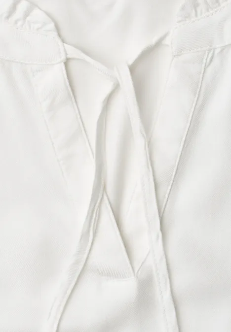Close-up van een wit bovenstuk met V-hals en decoratieve linten