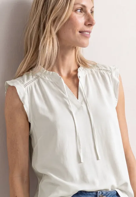 Mouwloze witte blouse met V-hals, fijne kanten details op de schouders en tunnelkoordjes.