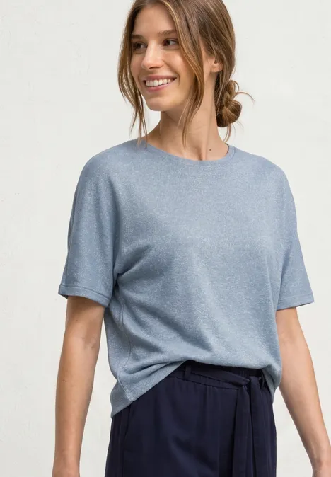 Frau in hellblauem T-Shirt und dunkler Hose vor neutralem Hintergrund
