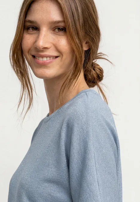 Nahaufnahme einer Frau in hellblauem Pullover, Haare locker im Dutt gebunden.