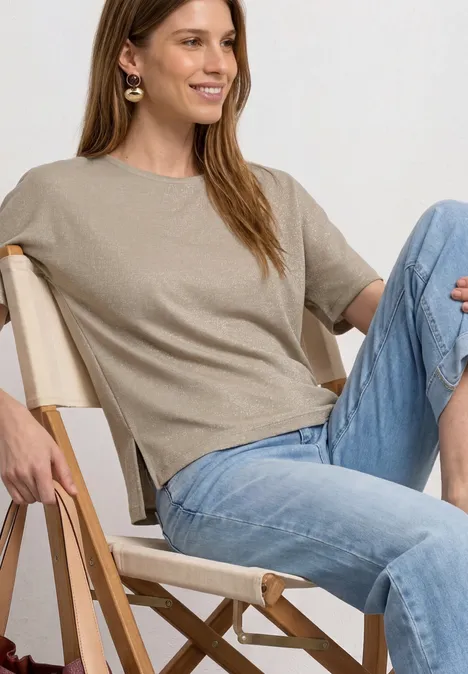 Frau sitzt entspannt auf Campingstuhl, trägt beigefarbenes T-Shirt und blaue Jeans.