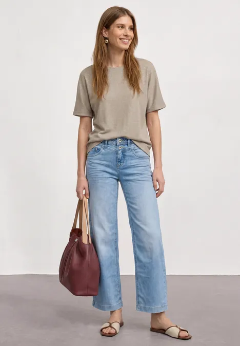 Frau mit grauem T-Shirt, hellblauen Jeans, schwarzen Sandalen und roter Handtasche.