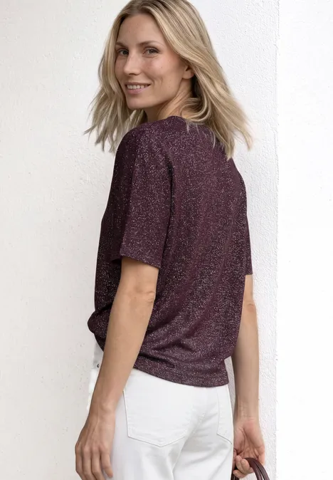 Een persoon van achter gefotografeerd draagt een glitter T-shirt en witte jeans voor een witte achtergrond.