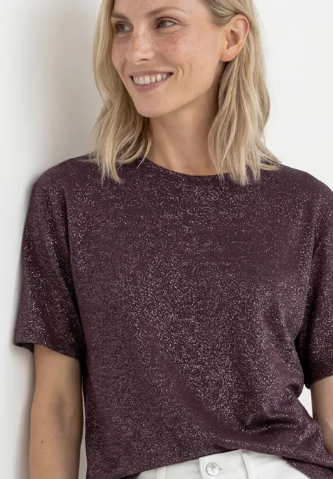 Vrouw in paars glinsterend T-shirt lacht voor een lichte achtergrond.