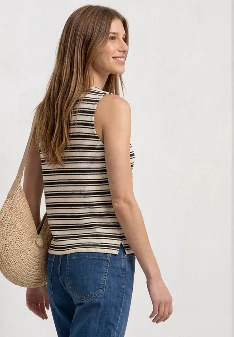 Frau mit gestreiftem Top, Jeans und Strohtasche, seitlich von hinten fotografiert.