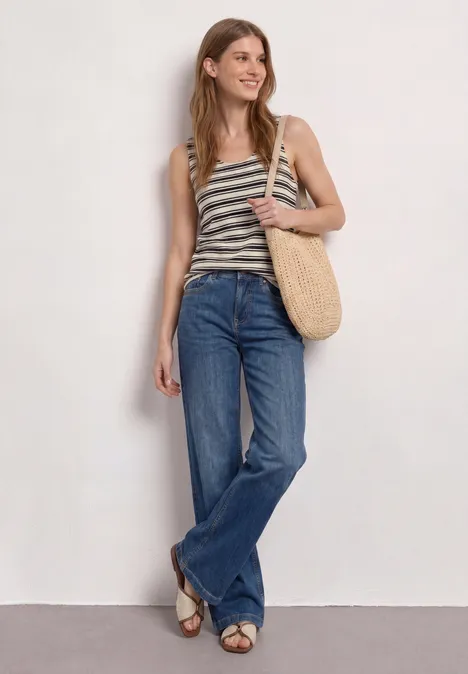Eine Frau trägt ein gestreiftes Top, weite Jeans und eine Korbtasche.