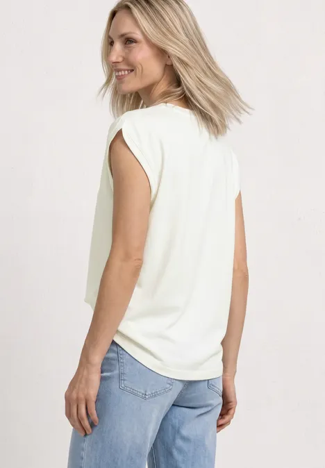 Eine Frau trägt eine weiße ärmellose Bluse und hellblaue Jeans, Rückansicht, Blick über die Schulter.