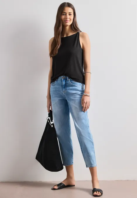 Frau in schwarzem ärmellosem Top, hellblauen Jeans und schwarzen Sandalen, trägt schwarze Handtasche.