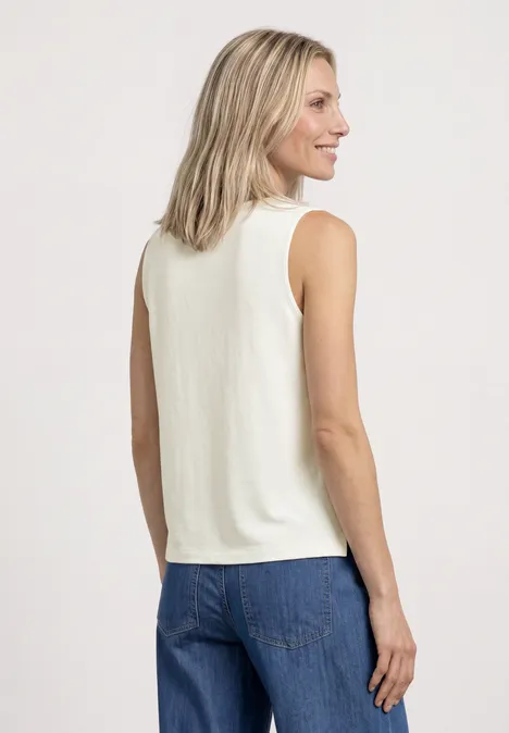 Eine Frau von hinten in weißem ärmellosem Top und blauen Jeans vor hellem Hintergrund.