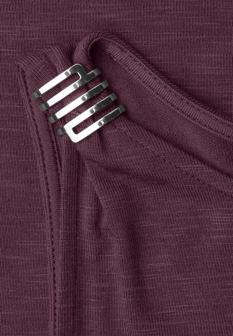 Nahaufnahme eines bordeauxfarbenen Shirts mit Brusttasche und daran befestigtem silbernen Metall-Clip.