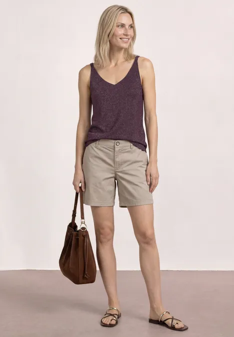 Top mit V-Neck und Glitzerdetails rustic rouge Frau in lila Top, beigen Shorts und Sandalen, hält eine braune Tasche.
