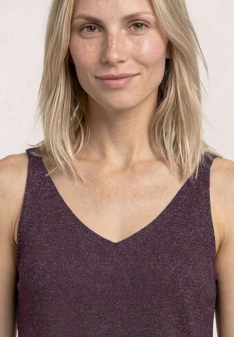 Top mit V-Neck und Glitzerdetails rustic rouge Frau mit schulterlangem blonden Haar trägt ein ärmelloses violettes V-Ausschnitt-Top vor hellem Hintergrund.