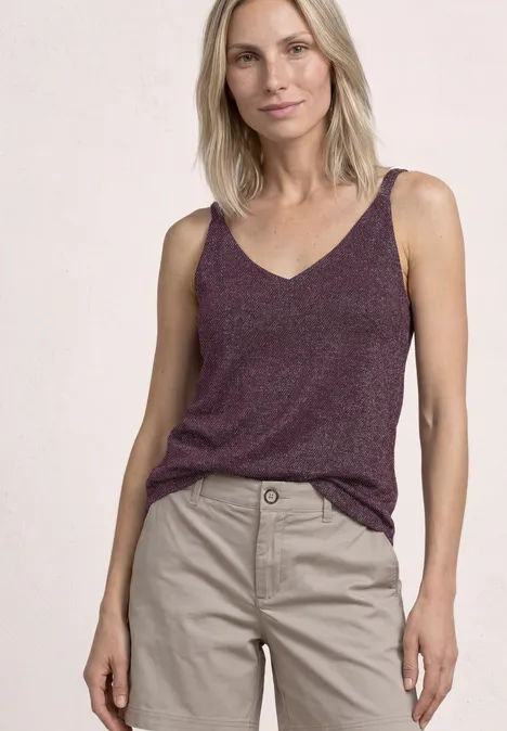 Top mit V-Neck und Glitzerdetails rustic rouge Frau trägt lila V-Ausschnitt-Top und beige Stoffhose, steht vor hellem Hintergrund.