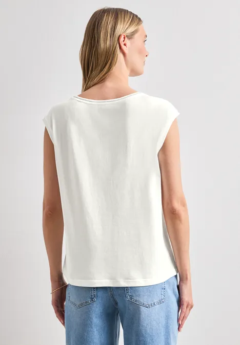 Hinteransicht einer Person in lockerem weißem T-Shirt mit überschnittenen Ärmeln und blauen Jeans vor grauem Hintergrund.