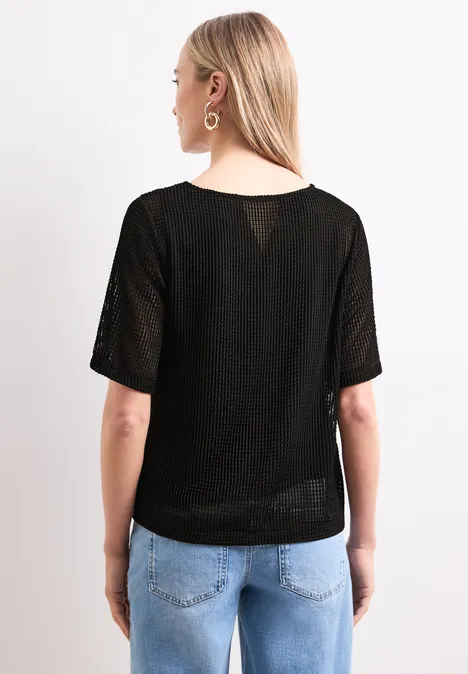 Rückansicht einer Frau mit hellem Haar, trägt schwarzes Shirt und blaue Jeans.