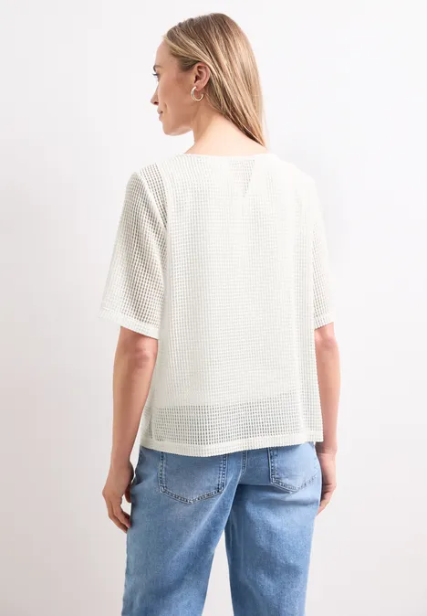 Rückenansicht einer Frau in weißer, leicht transparenter Bluse und blauen Jeans