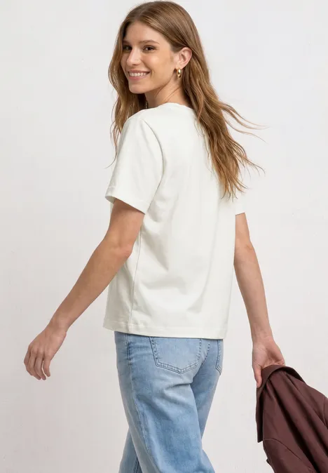T-Shirt mit Rundhals und Brusttasche off white Frau von hinten in weißem T-Shirt, Jeans, hält eine Jacke in der Hand.