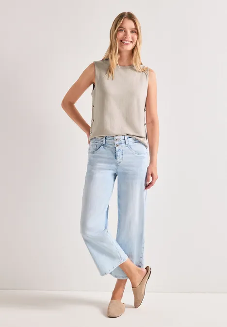 Vrouw in licht topje, lichtblauwe jeans en beige espadrilles voor een witte achtergrond.