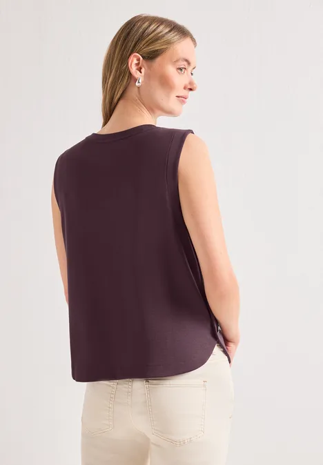 Frau von hinten trägt ein ärmelloses dunkelviolettes Top und helle Hosen.