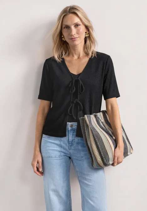 Veste en maille avec rubans Black Femme aux cheveux blonds porte un top noir à manches courtes, un jean bleu et un sac rayé.