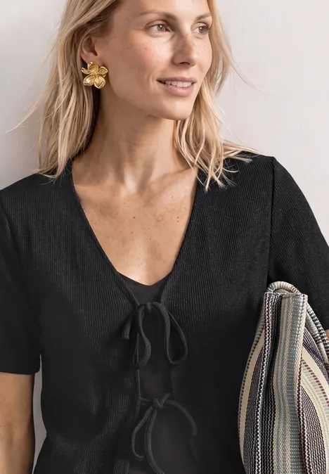 Veste en maille avec rubans Black Femme en haut noir à manches courtes et nouettes, portant un sac rayé couleur neutre.