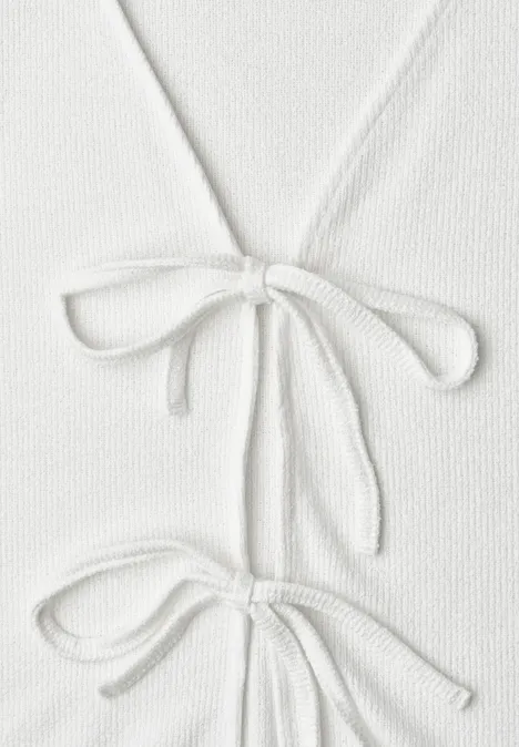 Veste en maille avec rubans off white Gros plan sur un vêtement en maille blanc avec deux rubans noués en nœuds.