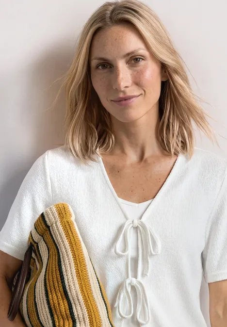 Veste en maille avec rubans off white Une personne porte un chemisier blanc à nœuds et tient un tricot rayé jaune et marron.