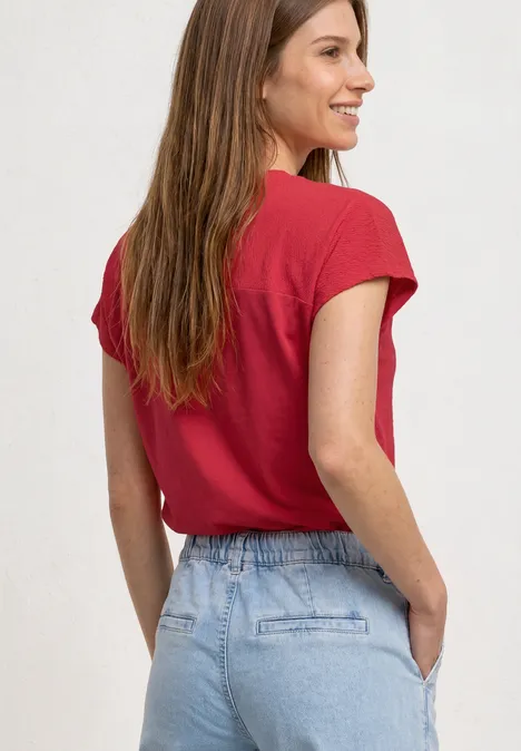 Frau in rotem T-Shirt und Jeans von hinten, Hände in den Taschen.