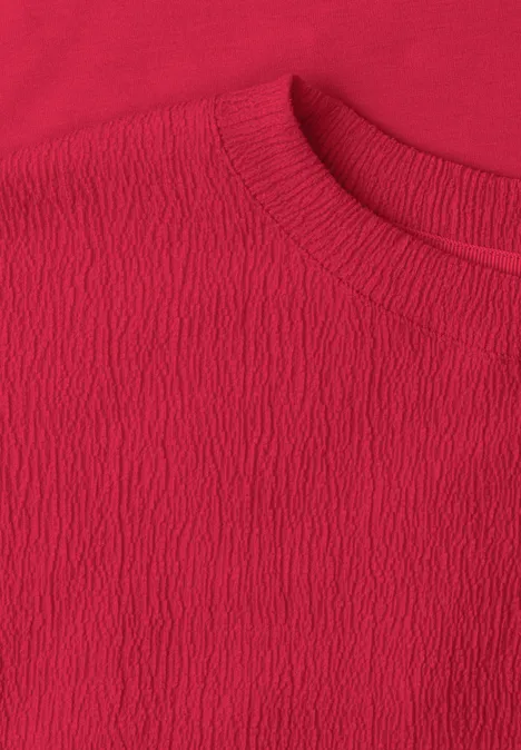 Nahaufnahme eines roten T-Shirts mit rundem Halsausschnitt und feiner, strukturierter Oberfläche.