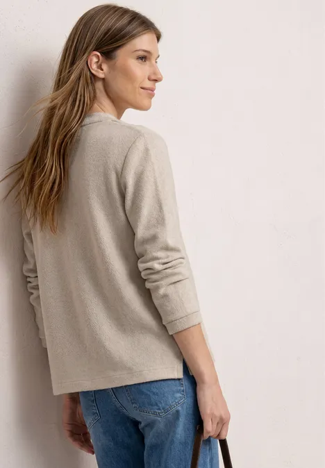 Achteraanzicht van een vrouw met beige trui en blauwe spijkerbroek voor een lichte achtergrond.