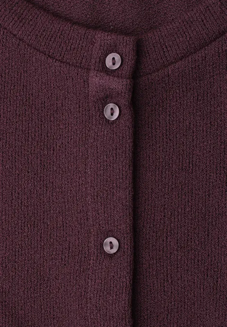 Close-up van een bordeauxrode gebreide cardigan met drie knopen aan de voorkant.