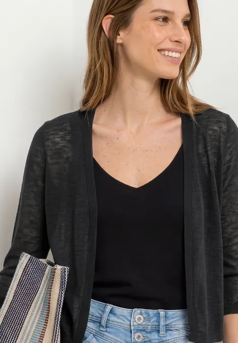 Frau mit schwarzem Top und dünner Cardigan, blauer Jeans und gestreifter Tasche.