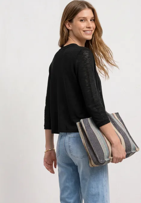 Frau im schwarzen Oberteil und blauen Jeans hält eine gestreifte Clutch unter dem Arm.