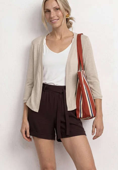Frau trägt weißen Top, beigen Cardigan, braune Shorts und eine gestreifte Tasche.