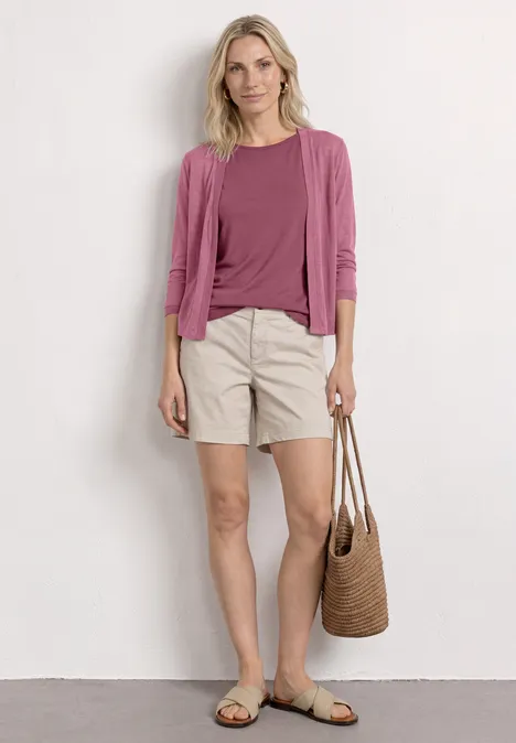 Femme en haut et gilet rose, short beige, sandales et sac en paille, look estival décontracté.