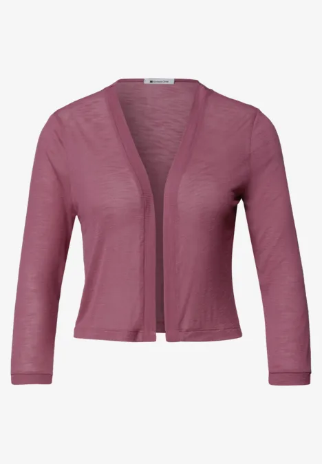 Un boléro court en tricot rose, manches 3/4, léger et ouvert sur le devant.