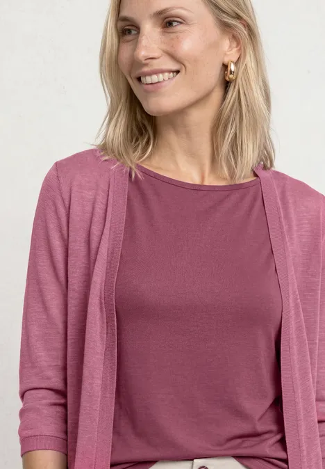 Femme blonde souriante portant un haut et un cardigan roses.