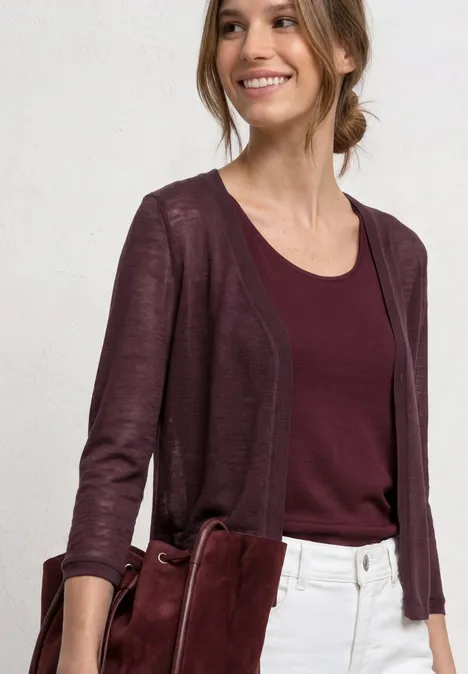 Frau in weißer Hose, bordeauxrotem Top und Cardigan, hält eine passende rote Tasche.