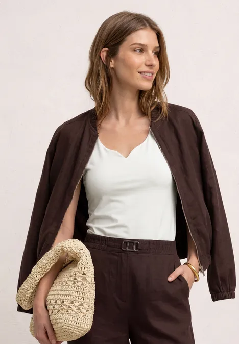 Vrouw met wit topje, bruine blazer en bijpassende broek, met een gevlochten rietentas.