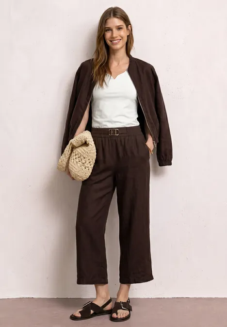 Vrouw in bruin oversized jasje en culotte, wit topje, zwarte sandalen en gevlochten tas