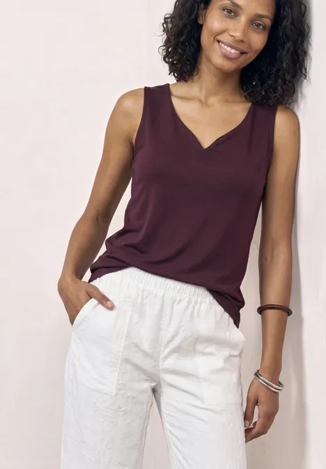 Basic top met hartvormige halslijn rustic rouge Eine Person trägt ein ärmelloses weinrotes Top und eine weiße Hose vor hellem Hintergrund.