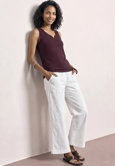 Basic top met hartvormige halslijn rustic rouge Eine Frau lehnt an einer Wand, trägt ein ärmelloses burgunderfarbenes Top, weiße Culotte und Sandalen.
