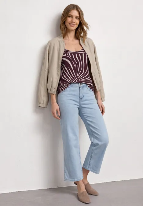 Une femme en top rayé, veste claire et jean large pose devant un mur neutre.