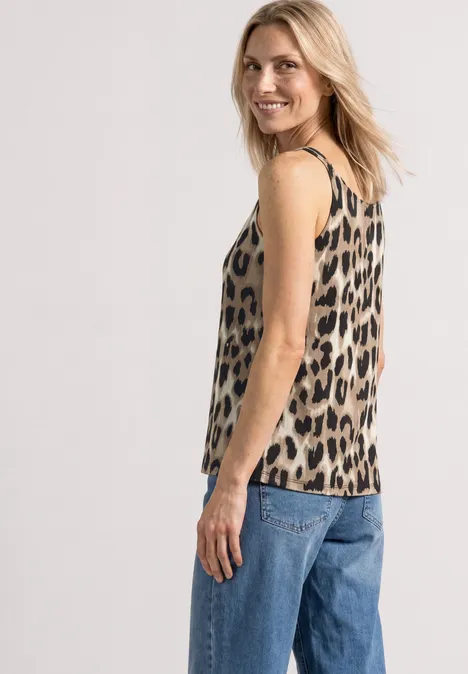 Femme de profil portant un top léopard sans manches et un jean bleu sur fond clair.