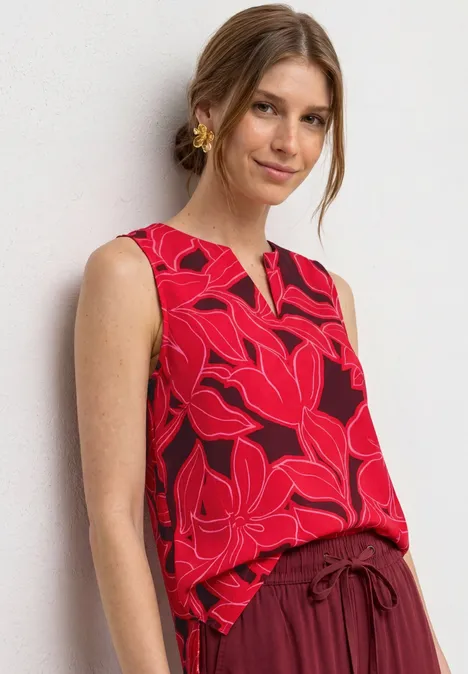 Vrouw met rood mouwloos topje met roze bloemenprint.