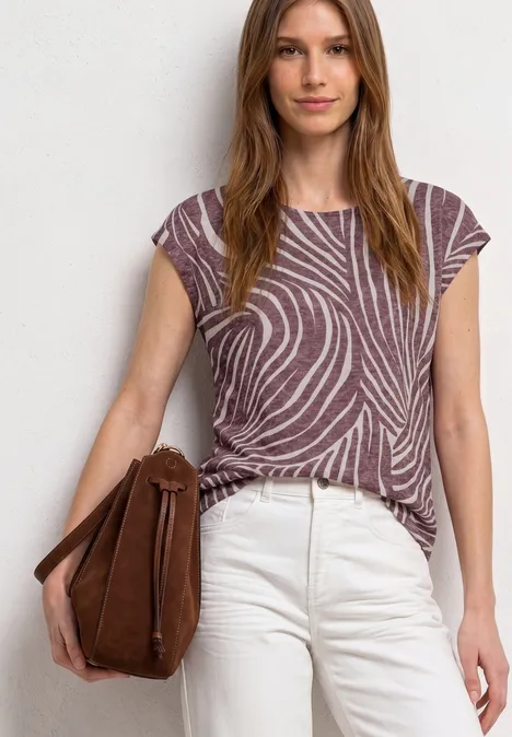 Personne portant un pantalon blanc et un haut violet à motifs, tenant un sac marron.