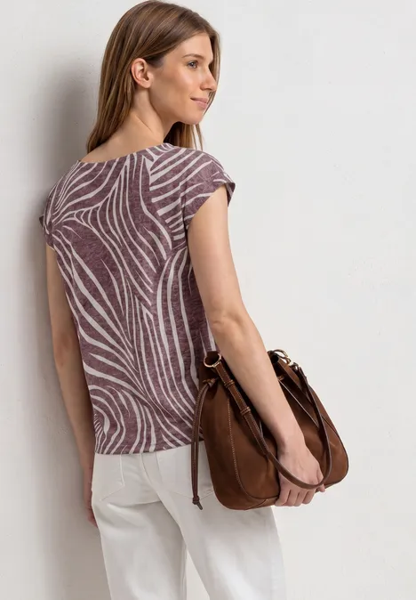 Femme de dos en blouse à motifs et pantalon clair, portant un sac marron à l'épaule.