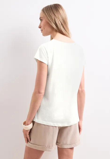Koszulka na ramiączkach z napisem off white Kobieta widziana od tyłu w białej koszulce i beżowych szortach.