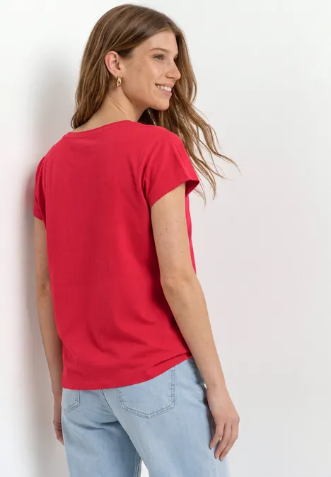 Dropped Shoulder Shirt mit Wording salsa red Frau von hinten in rotem T-Shirt und hellen Jeans vor weißem Hintergrund.