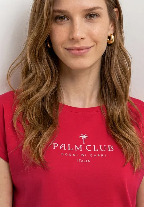 Dropped Shoulder Shirt mit Wording salsa red Person mit rotem T-Shirt „PALM CLUB FOOD & GRACE ITALIA“ und welligen, schulterlangen Haaren